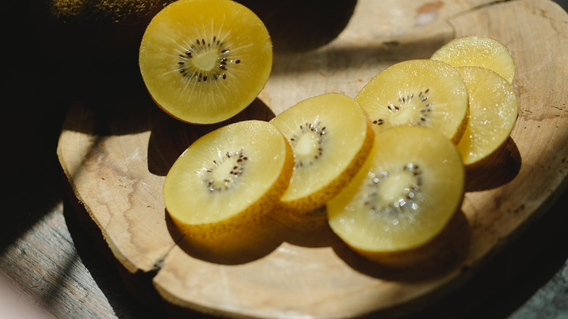 Eine aufgeschnittene, gelbe Kiwi auf einem Holzbrett.