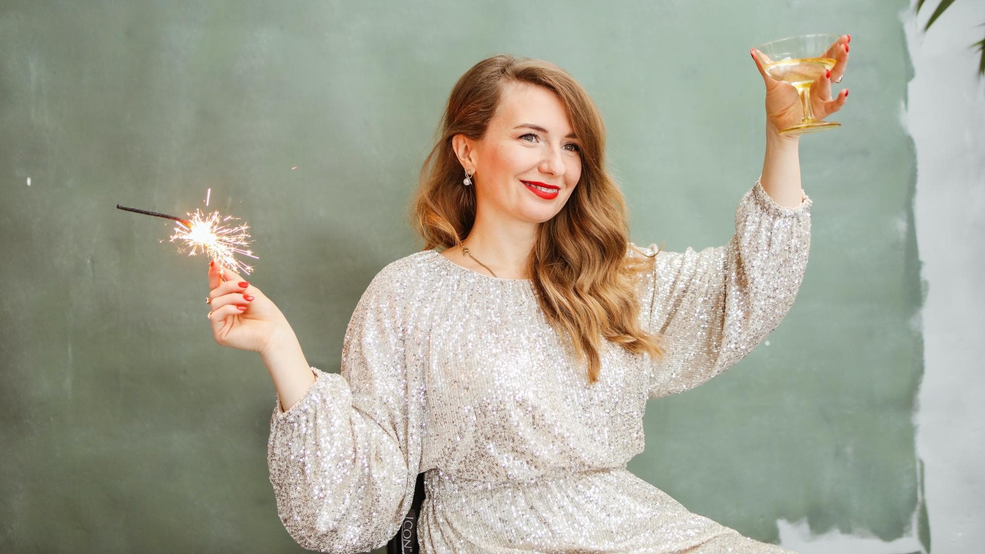 Frau mit Wunderkerze und einem Sektglas in der Hand.