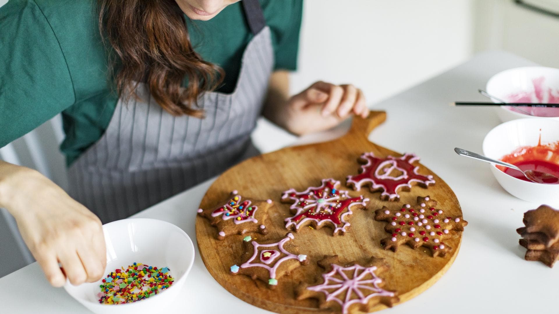 Frau verziert weihnachtliche Plätzchen mit Zuckerguss und bunten Streuseln.