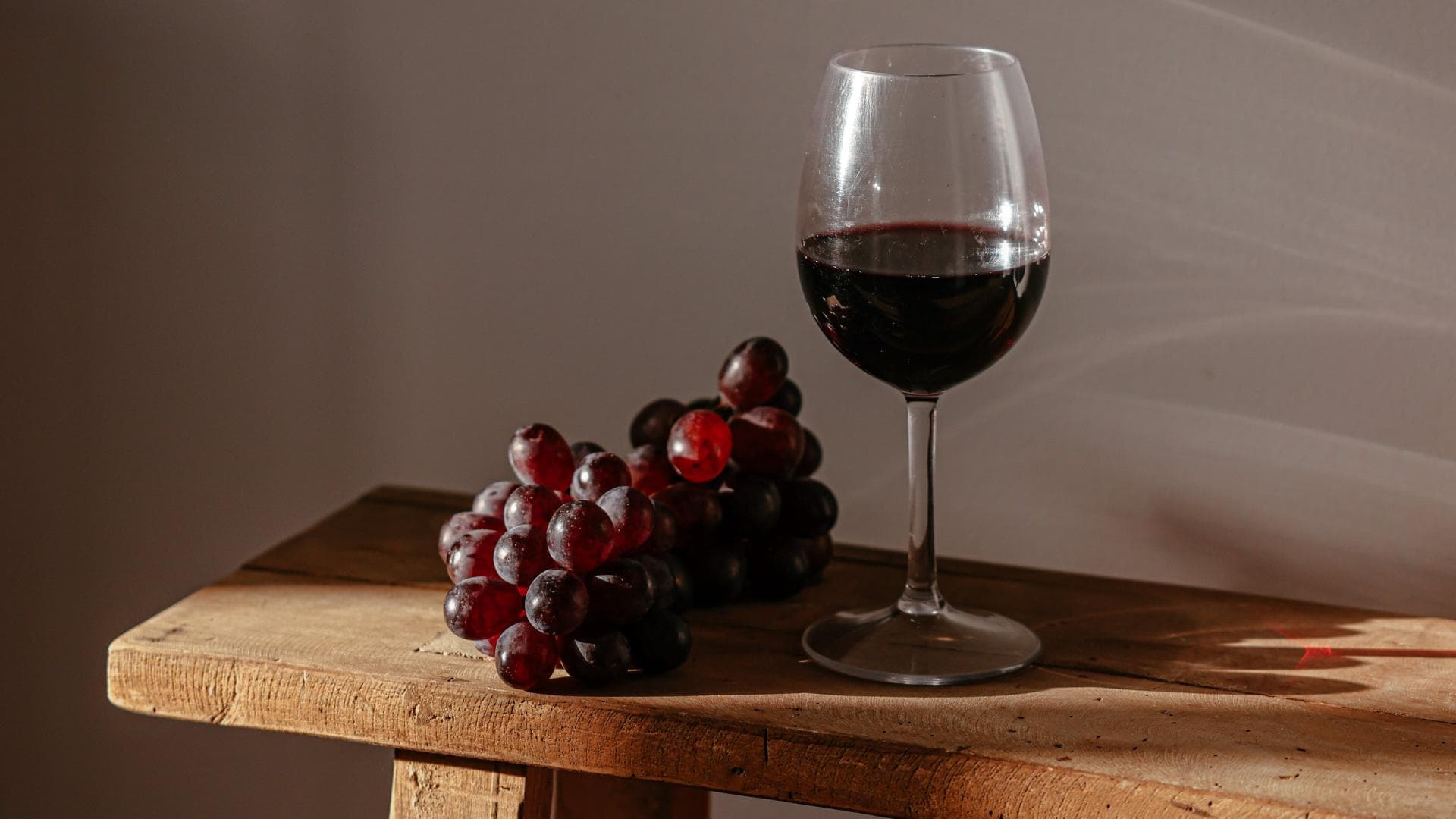 Ein Glas Rotwein und Trauben auf einer Holzbank.
