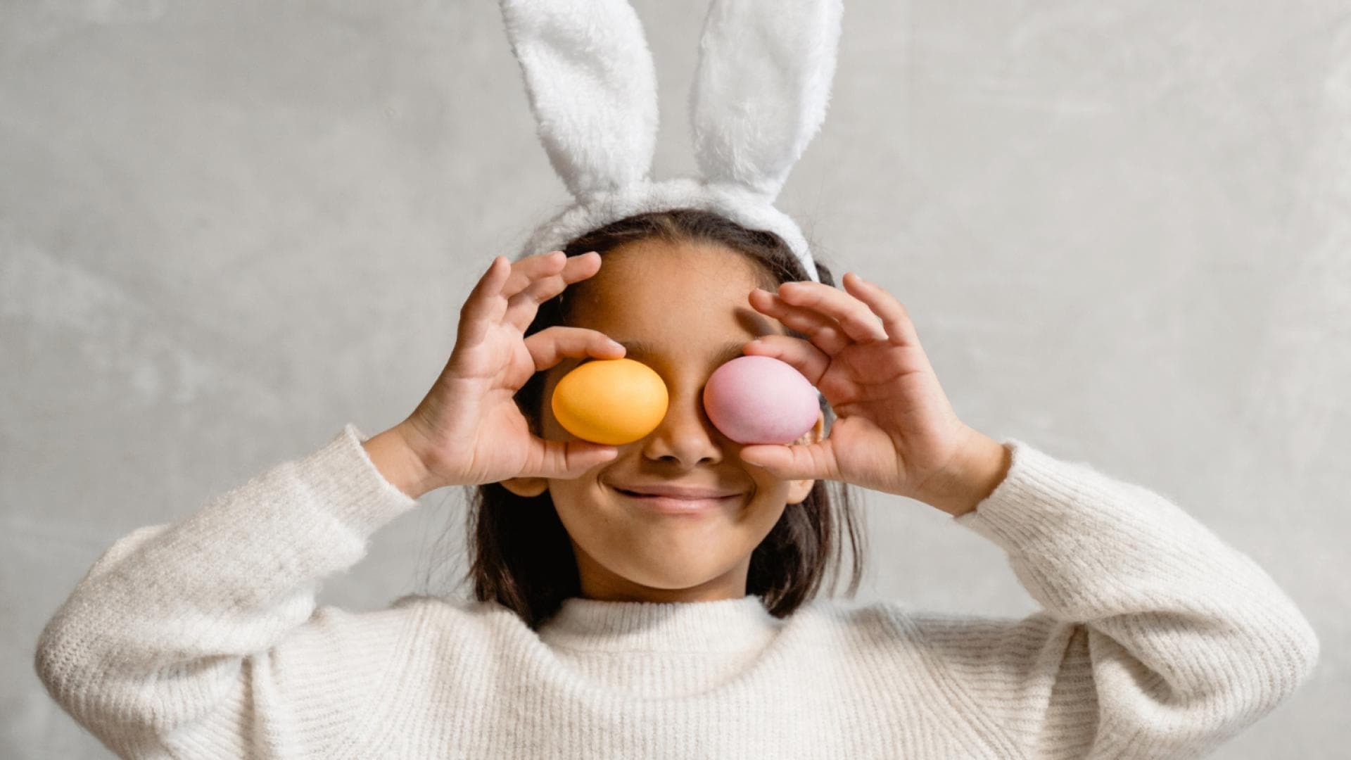 Kind mit Hasenohren hält sich zwei Ostereier vor die Augen