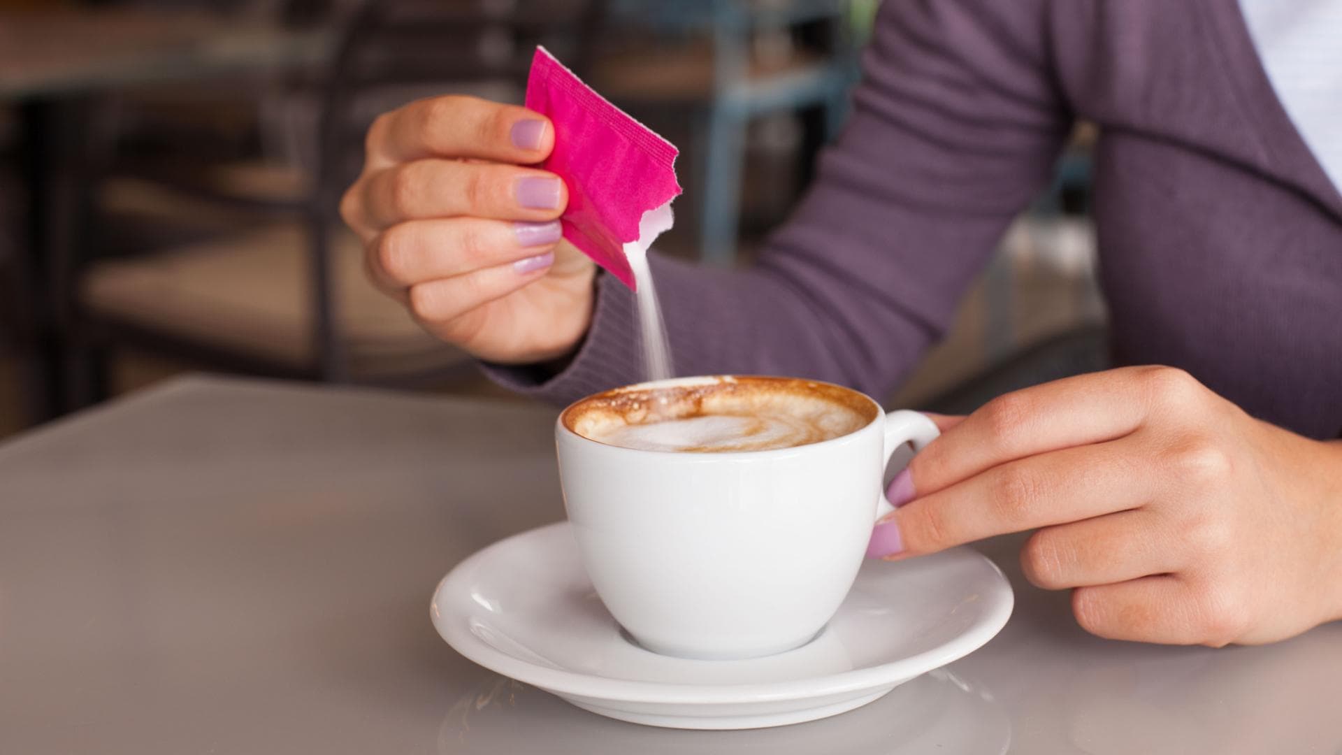 Frau schüttet Zucker oder Süßstoff in ihren Kaffee