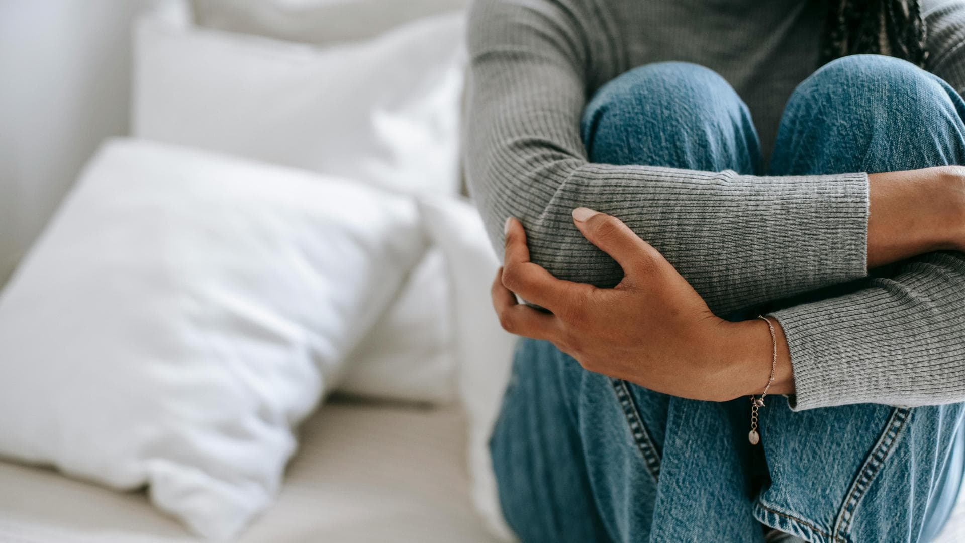 Frau sitzt auf Bett mit angezogenen Knien.