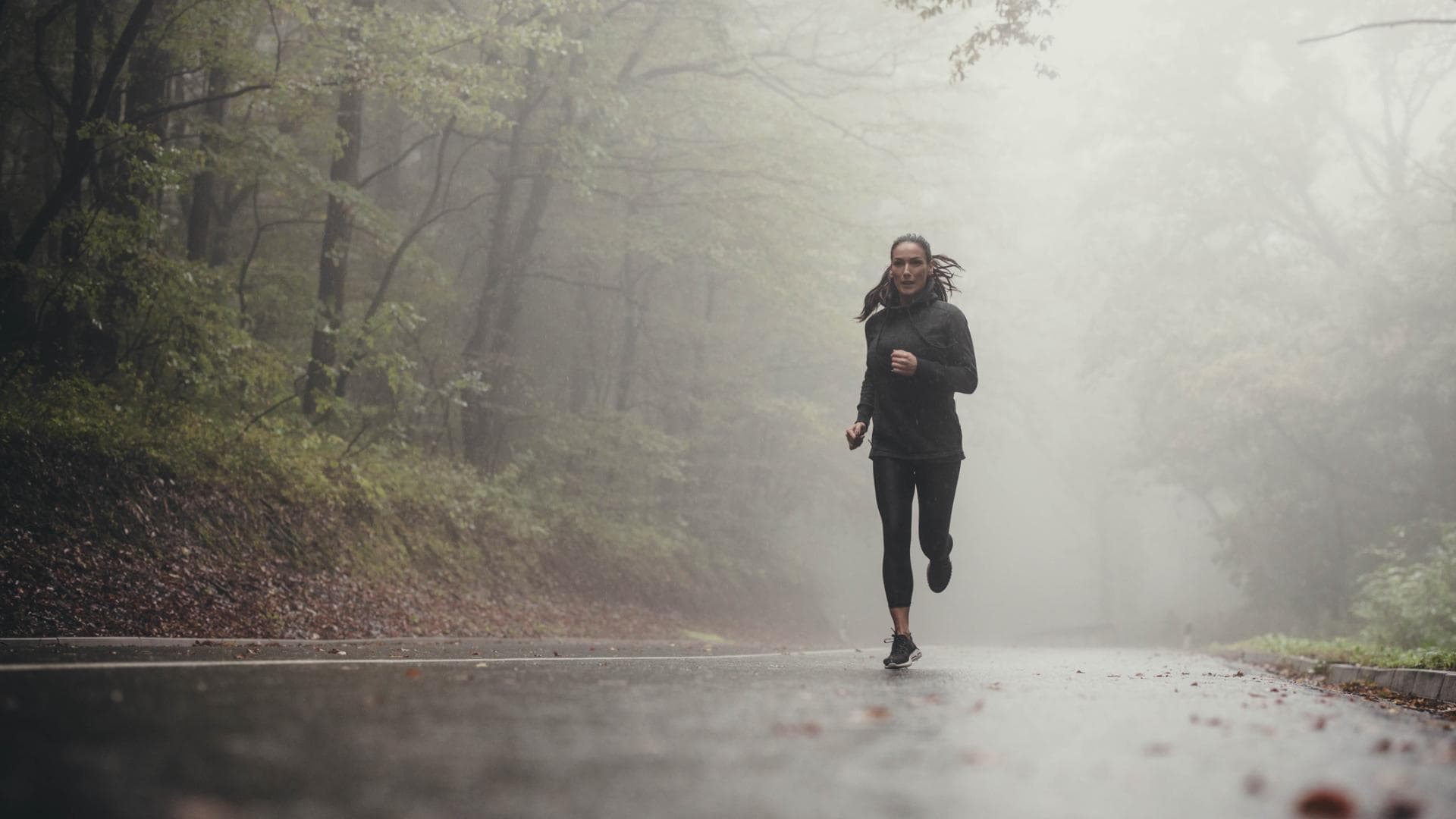 Frau beim Joggen bei Regen im Wald.