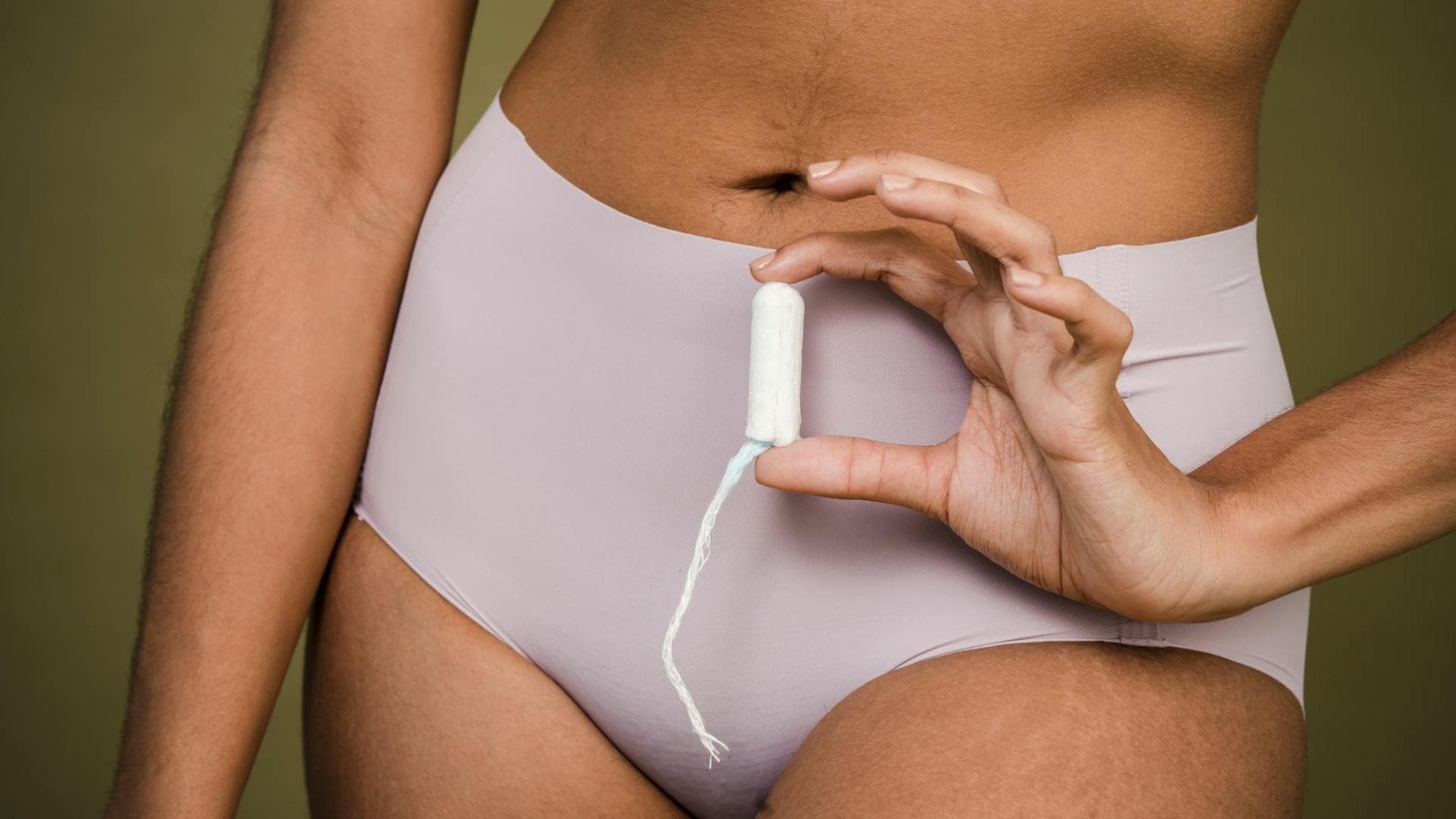 Frau hält einen Tampon vor ihrem Unterleib in der Hand.