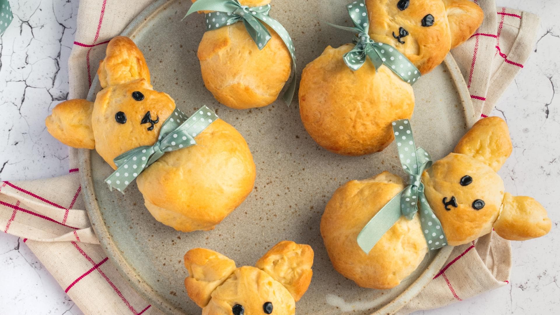 Fünf frisch gebackene Brioche-Häschen mit Schleife liegen auf einem Teller