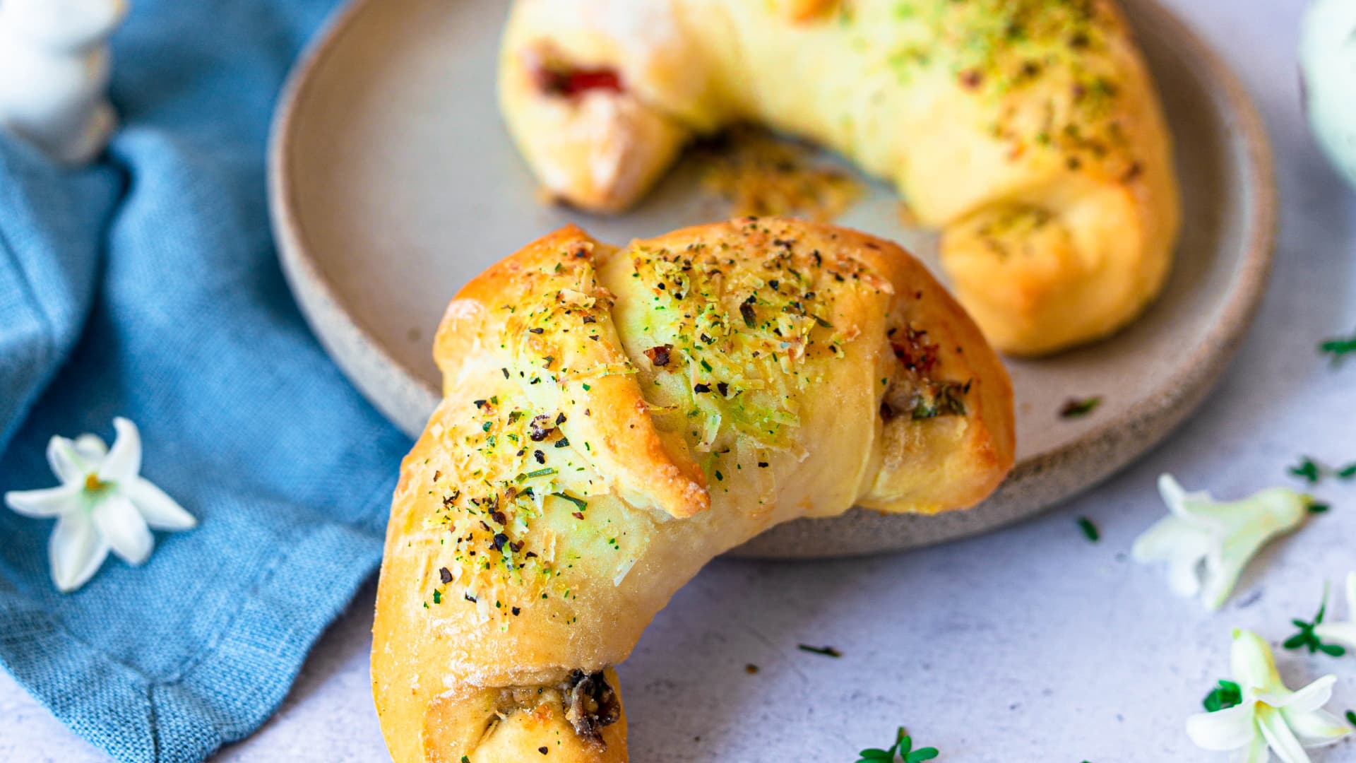 Pizzateig-Croissants mit Käse-Gewürz-Topping neben einem Teller angerichtet 