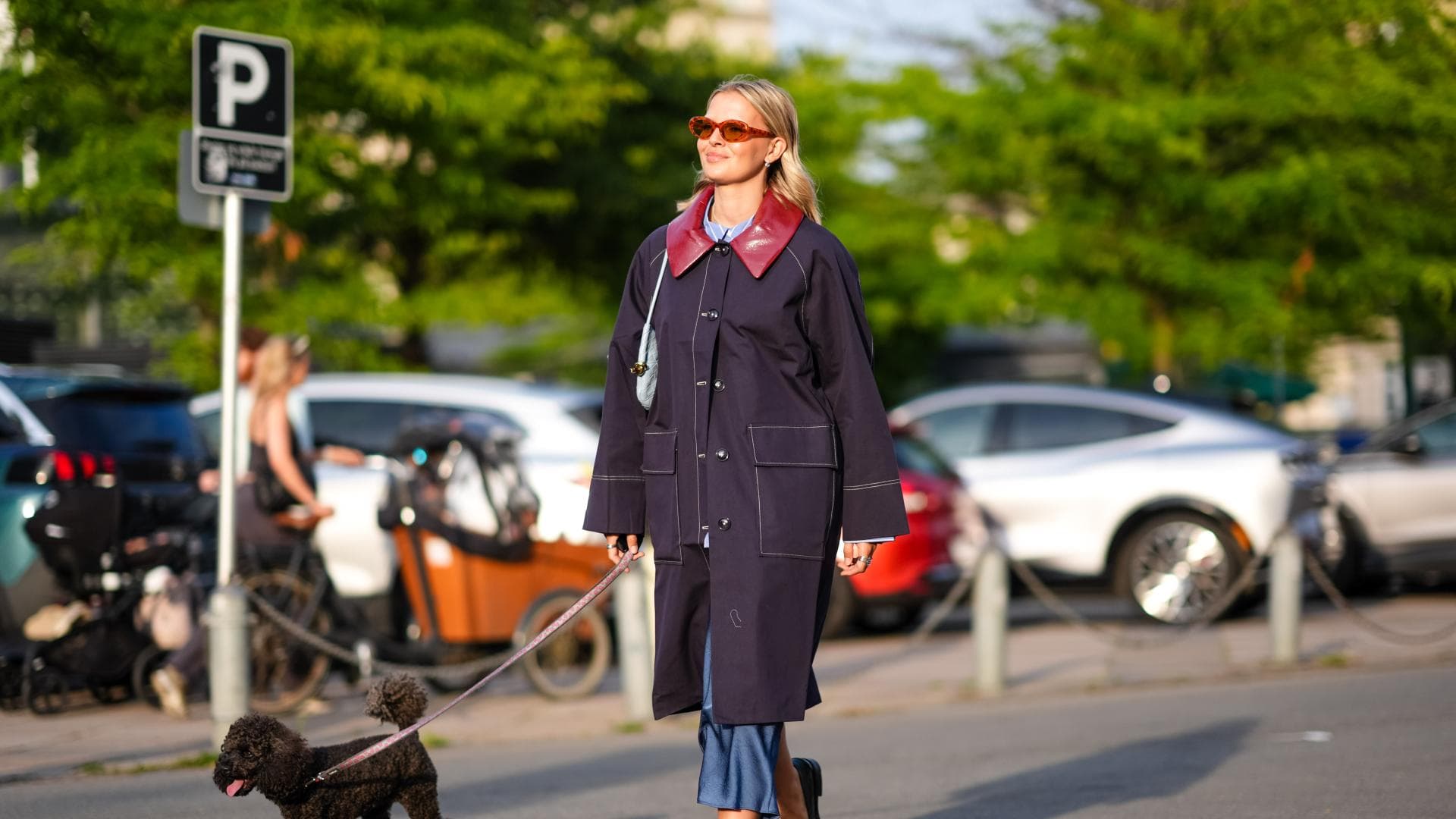 Eine blonde Frau, Mitte zwanzig, führt ihren Hund an einem sonnigen Frühlingstag in Kopenhagen durch die Straßen