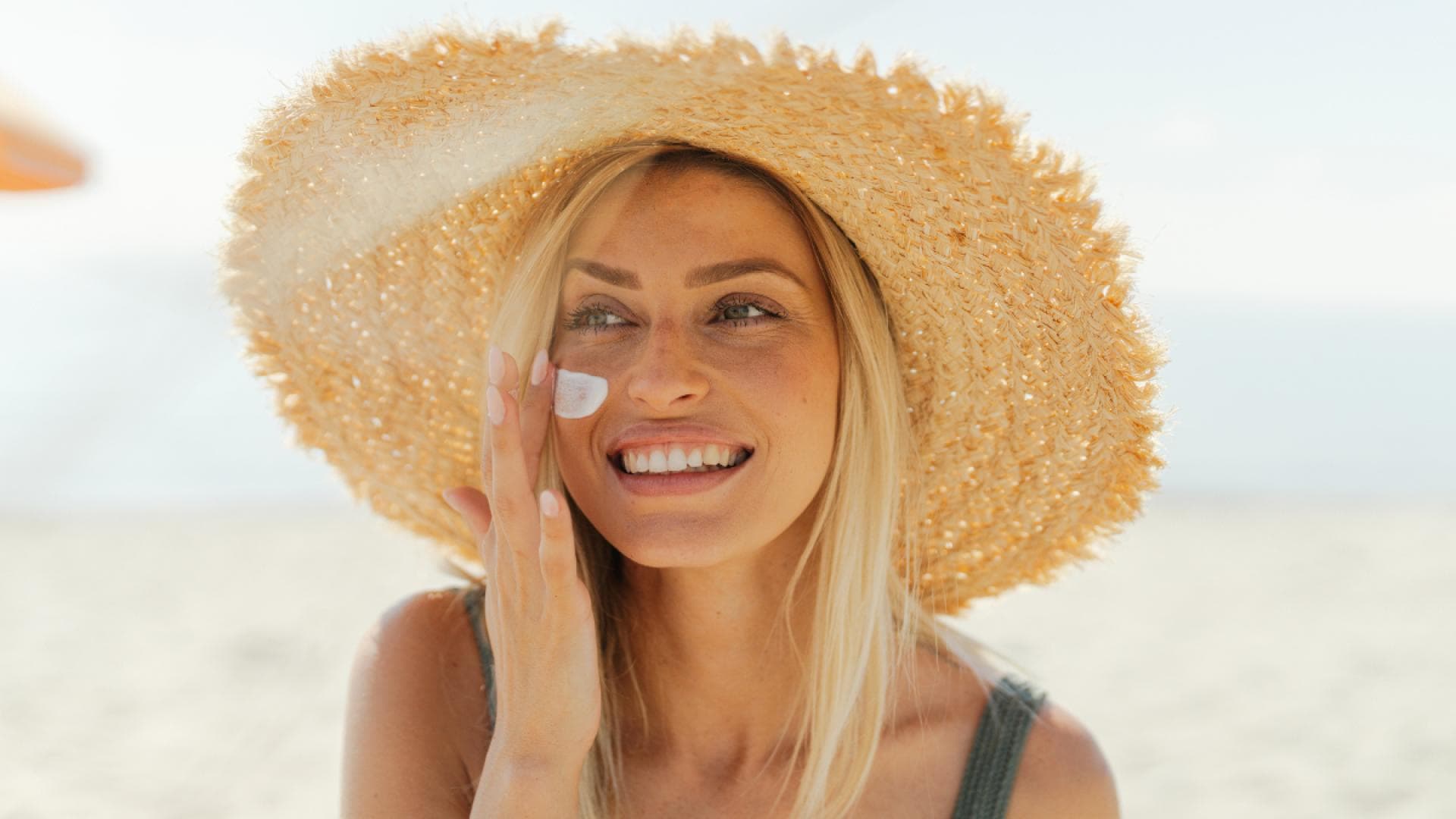 Frau mit Sonnenhut trägt Sonnencreme auf