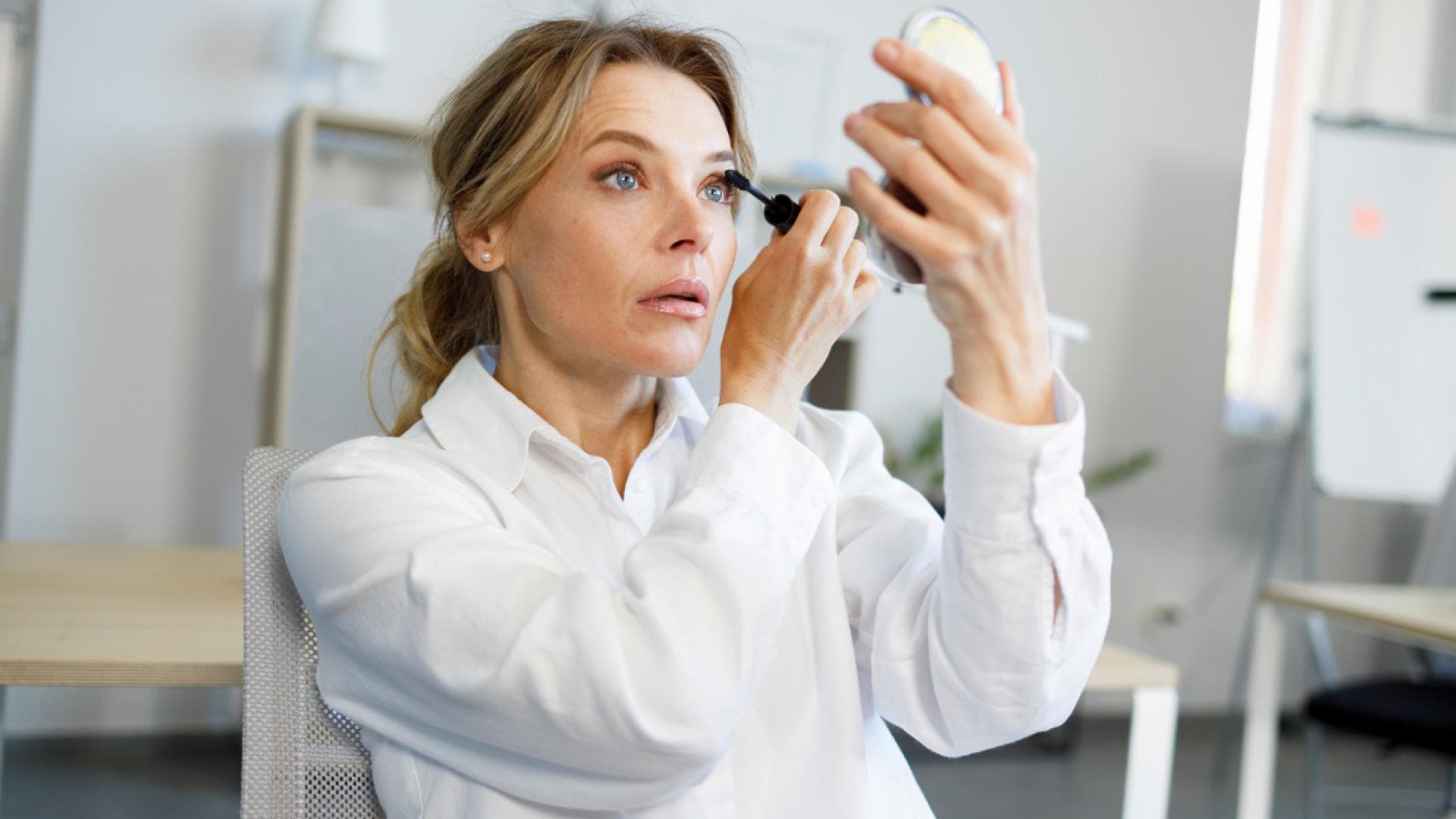 Frau tuscht Wimpern vor Handspiegel