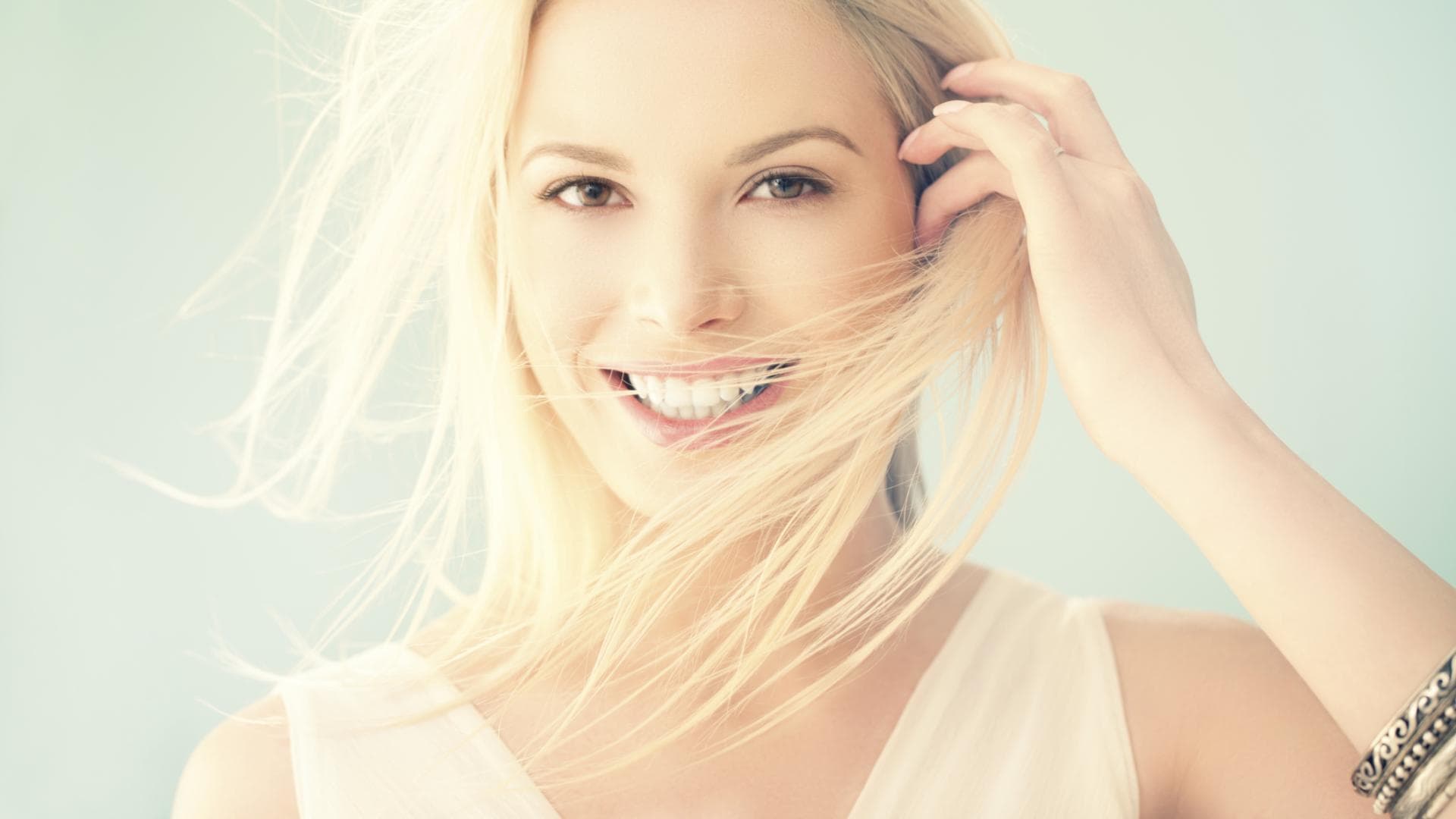 Eine Frau lächelt in die Kamera, ihre blonden Haare wehen im Wind