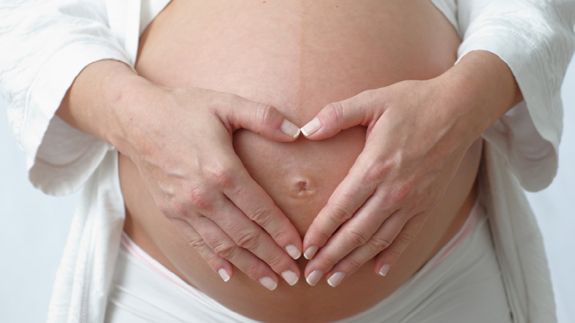 Eine hochschwangere Frau hält ihren Bauch. Sie erkennt erste Anzeichen einer bevorstehenden Geburt. 