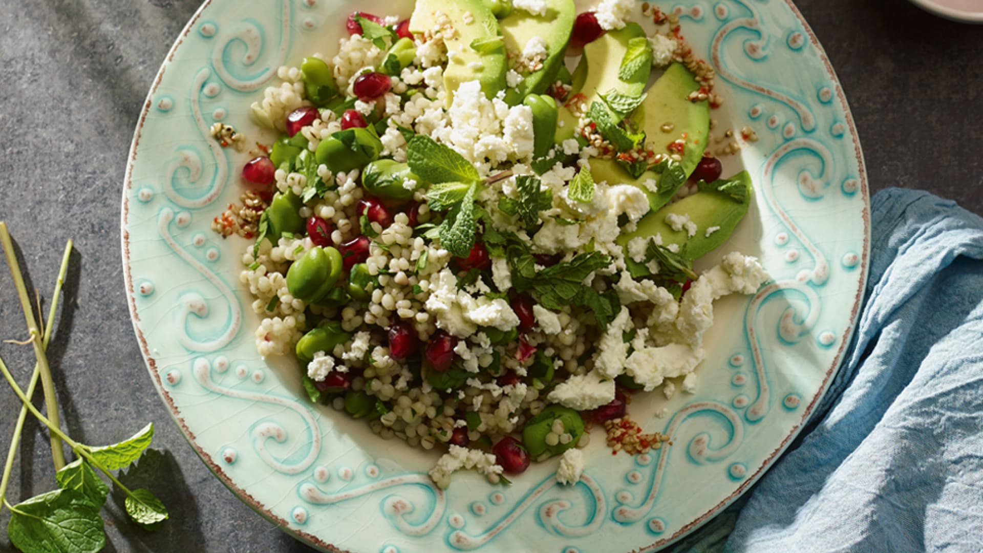 perlgraupensalat mit Granatapfel und Feta auf einem Teller, angerichtet mit Avocado