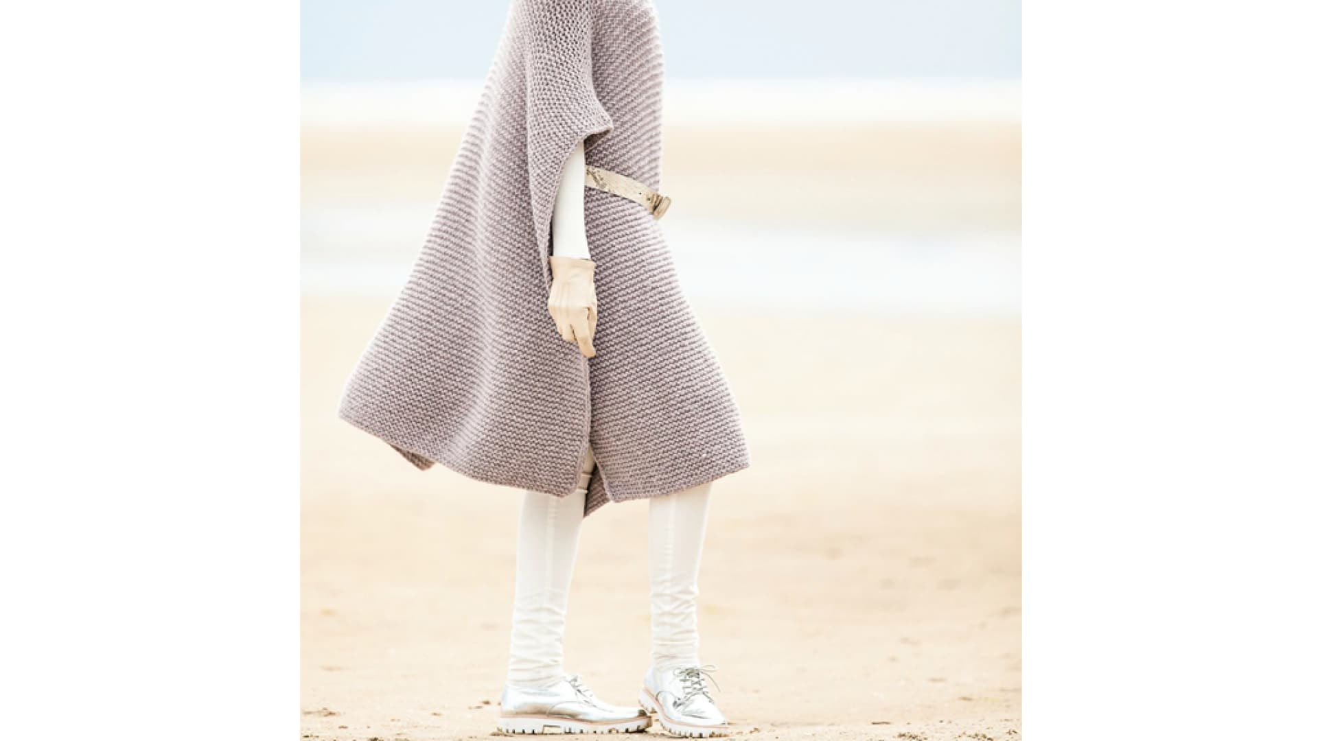 Frau trägt einen selbstgestrickten Wollponcho. Die Strickanleitung finden Sie bei uns.
