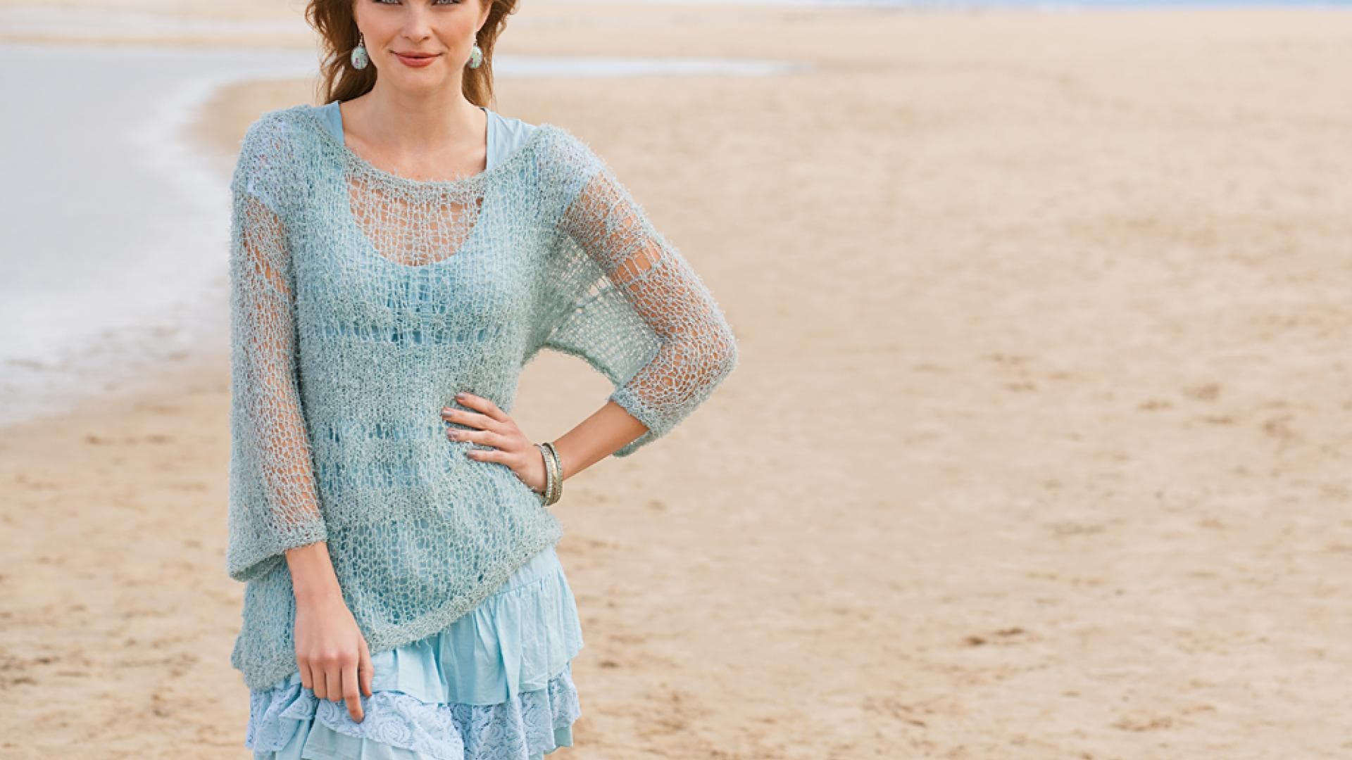 Frau mit transparentem Pulli in Mint steht am Strand