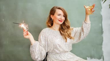 Frau mit Wunderkerze und einem Sektglas in der Hand.