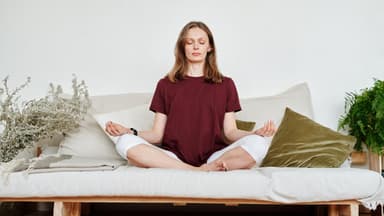 Eine Frau meditiert auf dem Sofa.