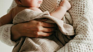 Frau hält ein Baby, das in eine Decke gehüllt ist.
