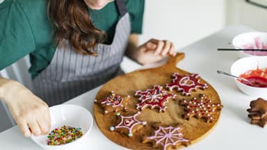 Frau verziert weihnachtliche Plätzchen mit Zuckerguss und bunten Streuseln.