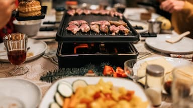 Ein Raclette-Gerät steht auf einer festlich gedeckten Tafel.