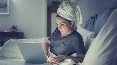 Frau am Laptop im Bett will mit nassen Haaren schlafen gehen