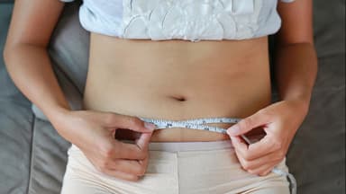 Frau liegt auf dem Rücken mit Maßband um den Bauch