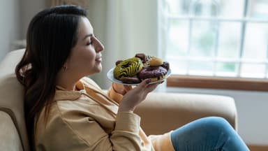 Frau hält einen Teller mit Donuts vor ihr Gesicht