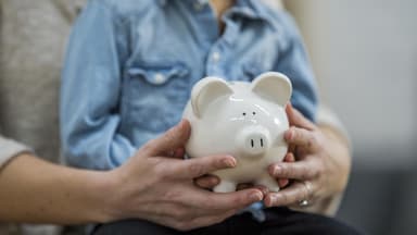Sparschwein in der Hand von einer Frau mit einem Kind auf dem Schoß