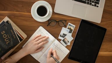 Frau schreibt etwas in ein Notizbuch neben ihrem Laptop