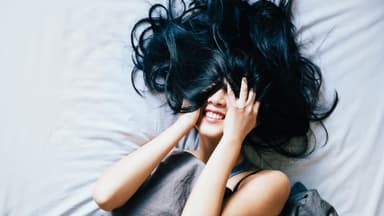 Frau liegt im Bett und hat ihre Haare im Gesicht