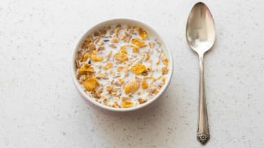Cornflakes mit Milch in einer Schüssel mit einem Löffel daneben