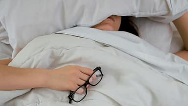 Frau liegt im Bett mit Kissen auf dem Kopf