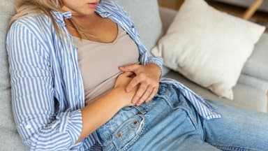Frau liegt auf dem Sofa und hält ihre Hände auf dem Bauch