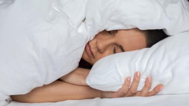 Frau liegt im Bett mit der Decke über dem Kopf