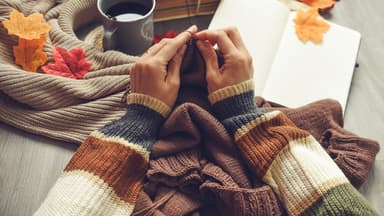 Frau strickt und hat ein Strickbuch parat
