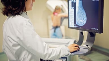 Eine Gynäkologin schaut sich das Bild einer Brust an, die gerade mithilfe einer Mammographie untersucht wird