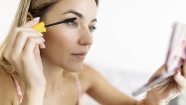 Frau tuscht Wimpern mit Handspiegel