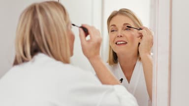 Frau tuscht ihre Wimpern vor Spiegel