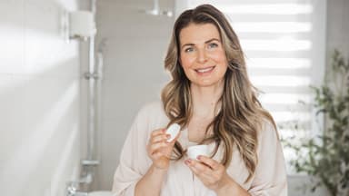 Frau im Bad mit Creme-Tiegel in der Hand