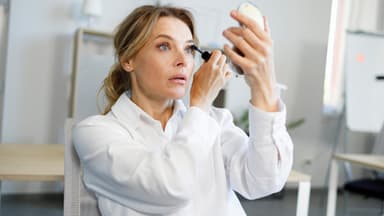 Frau tuscht Wimpern vor Handspiegel