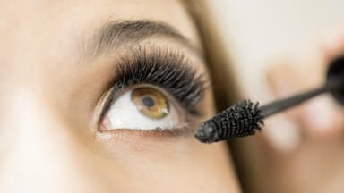 Frau trägt mascara für dichte Wimpern auf