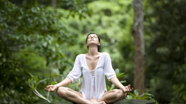 Eine Frau macht den Yoga Lotus-Sitz in einem grünen Wald