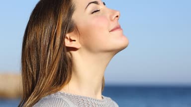 Eine Frau streckt das Gesicht der Sonne entgegen und atmet tief durch