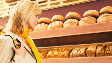 EIne blonde Frau sucht sich ein Brot aus dem Brotregal aus