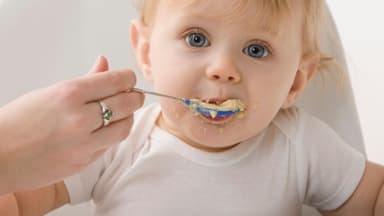 NIedliches blondes Baby wird mit Brei gefüttert