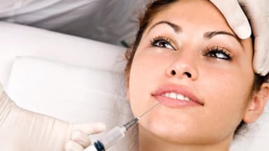 Frau bekommt auf einem Arztstuhl Botox gespritzt