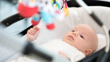 Baby liegt im Kinderwagen und schaut seine Kinderwagenkette