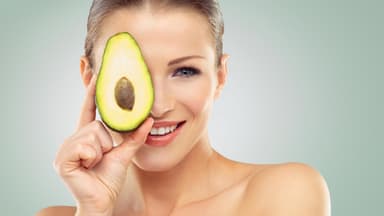 Diese Lebensmittel gelten als Fatburner: Frau hält Avocadohälfte