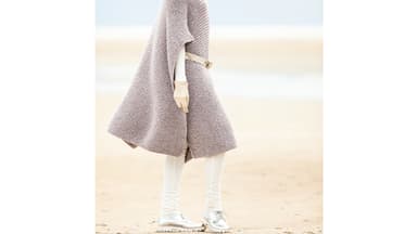 Frau trägt einen selbstgestrickten Wollponcho. Die Strickanleitung finden Sie bei uns.