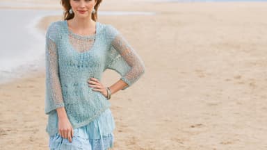 Frau mit transparentem Pulli in Mint steht am Strand